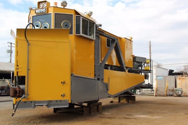 Large custom-fabricated yellow steel rail equipment staged in a yard
